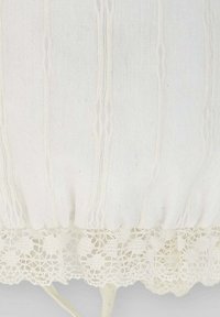 Indumento in tessuto bianco con texture a coste verticali, caratterizzato da un bordino in pizzo nella parte inferiore. Materiale morbido e leggero, dall'aspetto liscio.