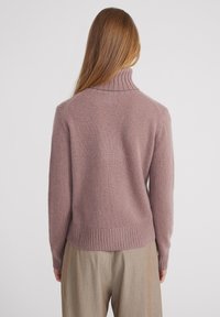 Helllila Pullover mit hohem Rippkragen, weicher Textur und geripptem Saum. Kombiniert mit hellen, plissierten Hosen.