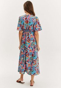 Maxi šaty z lehkého materiálu s vícolorovým listovým vzorem na modrém pozadí, se smyčkovým pasem a krátkými rukávy.