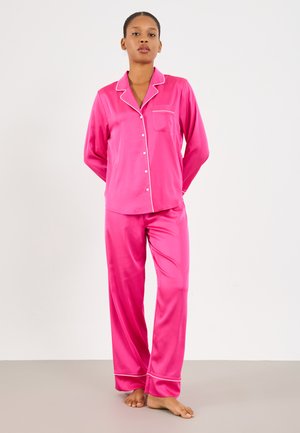 Ensemble de pyjama en satin rose avec des manches longues, un liseré blanc et une poche sur la chemise. Le pantalon est ample avec un liseré similaire aux poignets.