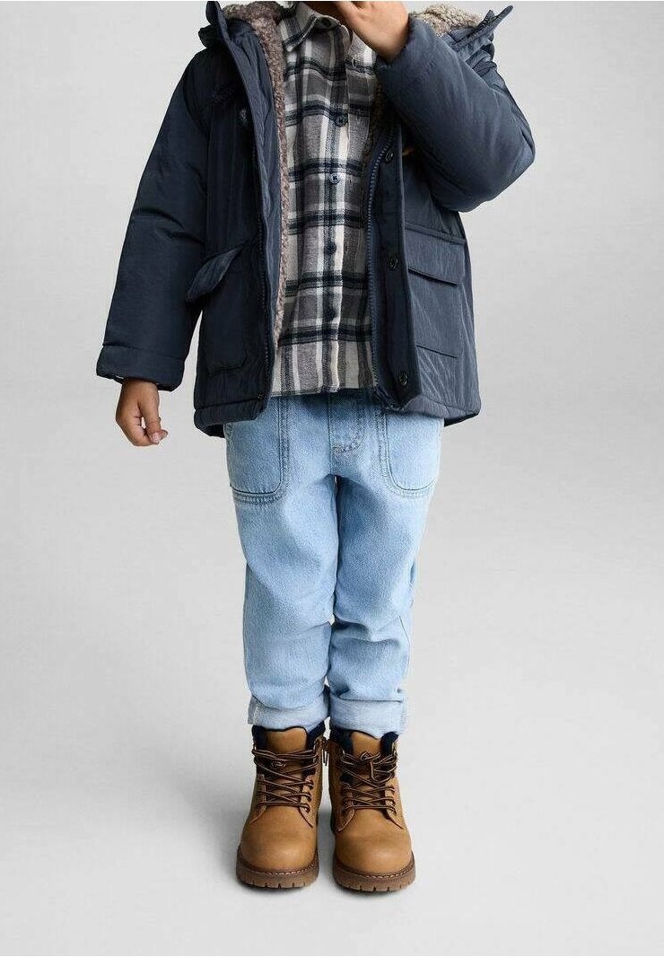 Doudoune marine avec doublure en fausse fourrure, chemise à carreaux grise et noire, jean en denim bleu clair et bottes en cuir marron à lacets.