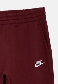 Bordové Nike tepláky so štruktúrovaným pásom, bočnými vreckami a bielym vyšitým logom na ľavom stehne.