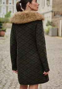 Cappotto in lana verde scuro con motivo a rombi, dotato di colletto in eco pelliccia marrone. Maniche lunghe e design di lunghezza media, adatto per il clima fresco.