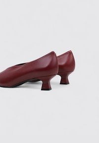 Chaussures en cuir bourgogne avec un bout arrondi et un petit talon évasé, dotées d'une texture lisse et d'un design minimaliste.