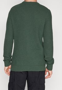 Pull vert foncé en tricot avec un motif texturé, col rond, manches longues et poignets côtelés. Design décontracté pour un usage quotidien.