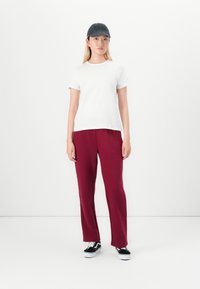 T-shirt bianca a maniche corte, pantaloni bordeaux, cappellino nero, scarpe nere. Design semplice con una vestibilità comoda e una texture morbida. Stile minimalista.