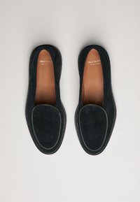 Suede loafers in dark navy with a rounded toe and contrasting stitched detailing. Leather insoles visible, minimalistic design and shape.