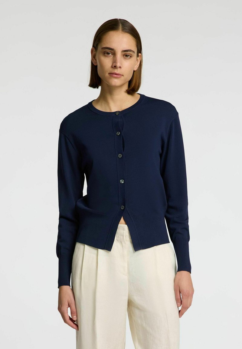 Marineblå cardigan med lange ærmer, rund halsudskæring, knapper foran og en let cropped design. Glat striktekstur og minimal detaljering.