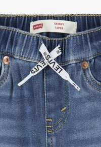 Los jeans skinny taper de Levi's en denim azul cuentan con una etiqueta tejida en el interior de la cintura y costuras en contraste. Incluyen un acento de botón metálico.