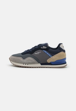 Sneaker blu navy e grigia con materiali in suede e mesh, caratterizzata da un accento color tan chiaro, dettagli blu e suola in gomma texturizzata.