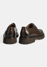 Chaussures en cuir marron avec une texture lisse, bout arrondi et semelle en caoutchouc épaisse dotée d'un design à motif. Surpiqûres accentuant près du talon.