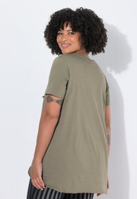 Camiseta de algodón verde oliva con un corte relajado, mangas cortas y dobladillo redondeado. Detalle notable: acento en la manga con una pequeña hendidura.
