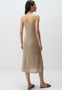 Beige gebreide jurk met een subtiele zigzagpatroon, spaghettibandjes en een middellange snit. Zachte textuur en doorschijnende details langs de zoom.