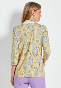 Gele blouse met paisley- en bloemenpatronen. Heeft driekwartmouwen en een soepele textuur. Afgewerkte zoom met een ontspannen pasvorm.
