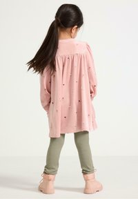 Abito di velluto rosa con ricami floreali, maniche lunghe e schiena arricciata, abbinato a leggings verde a coste e stivaletti alla caviglia rosa chiaro.