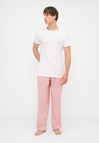 Valge puuvillane t-särk, millele on sobitatud punase ja valge triibulised pidžaama püksid, millel on mugav lõige ja sirge jala disain.