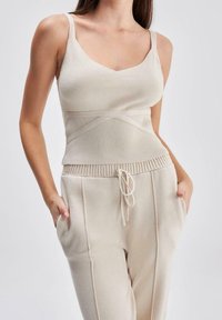 Bežové žebrované tílko s širokými ramínky, které má přiléhavý pas a bezešvý design; v kombinaci s odpovídajícími tepláky na gumu s bočními kapsami.