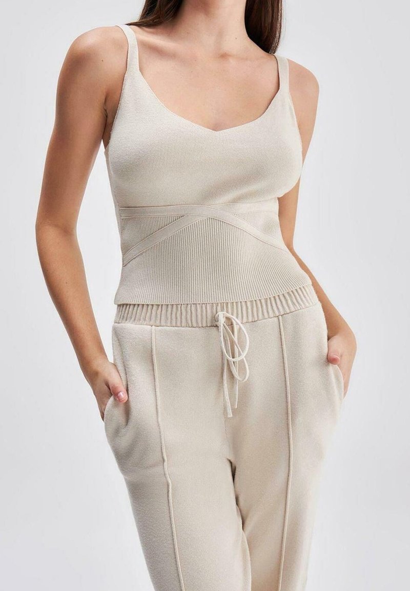 Bežové žebrované tílko s širokými ramínky, které má přiléhavý pas a bezešvý design; v kombinaci s odpovídajícími tepláky na gumu s bočními kapsami.