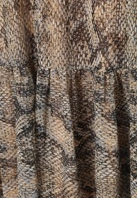 Detailný záber na zhrnutú látku so vzorom hadej kože v hnedej, béžovej a čiernej farbe, zobrazujúci detailnú textúru a šitie.