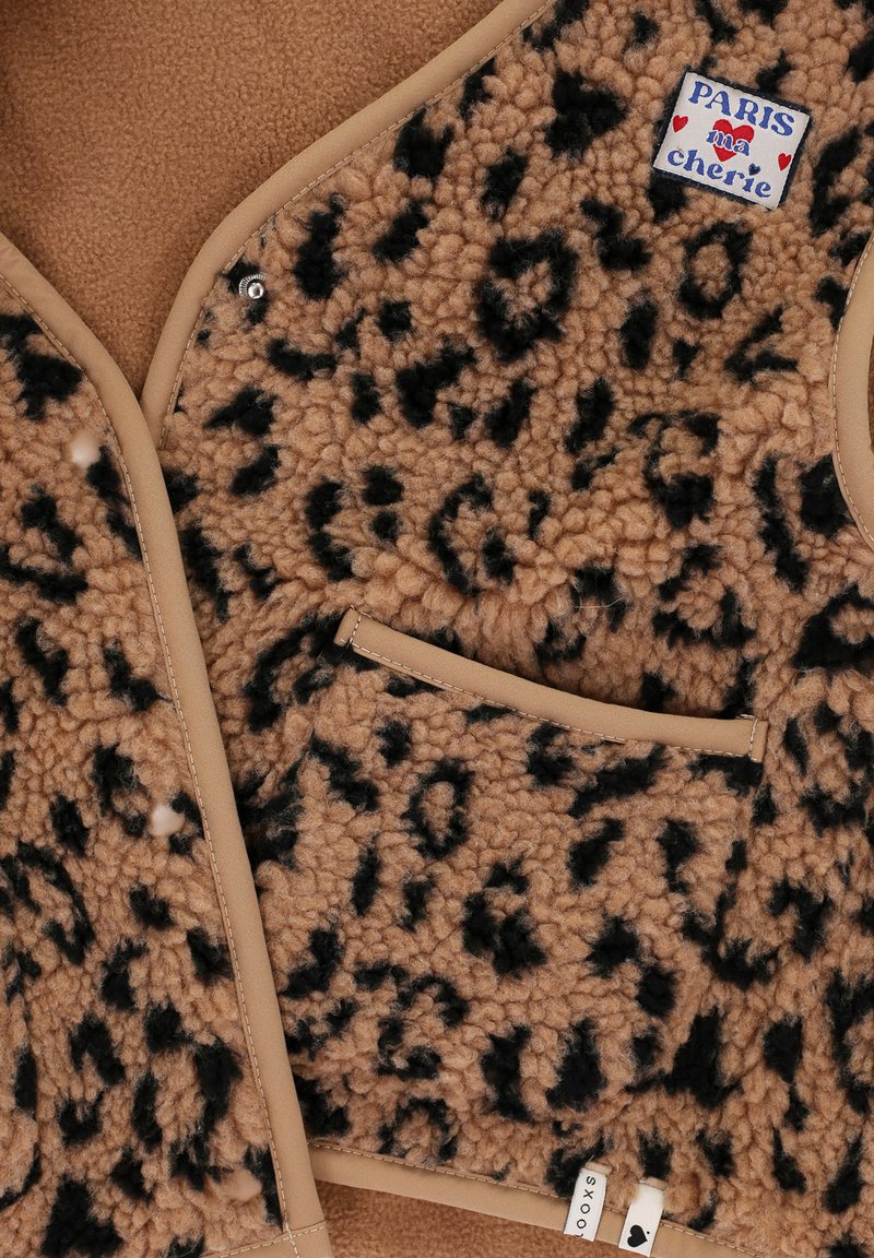 Beige en zwart gevlekte fleecevest met een tan afwerking, voorzien van een label met de tekst "Paris ma chérie" en een klein voorvakje.