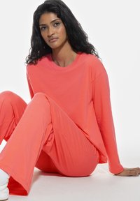 Korallfärgad loungewear-set bestående av en lös, långärmad skjorta och vida byxor. Mjuk, lättviktig tyg med en slät textur.