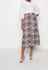 Haut court à col blanc avec manches bouffantes, associé à une jupe midi à motifs floraux en violet, bleu et noir. Mules argentées.