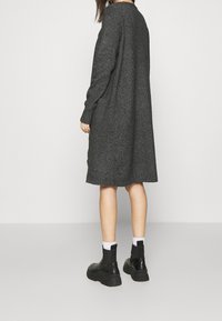 Šedé pletené šaty s dlouhým rukávem a volným střihem, s kulatým výstřihem a surovým lemem. Nosí se s černými kotníkovými botami a bílými ponožkami.