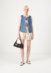 Jeansvest med frynser, hvit crop top, beige blonde shorts, svart skinnveske og lyse flate sko. Enkelt design og uformell stil.