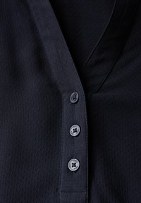 Maglietta nera a maniche corte con scollo a V, realizzata in tessuto testurizzato, con tre bottoni al colletto e dettagli di cucitura discreti.
