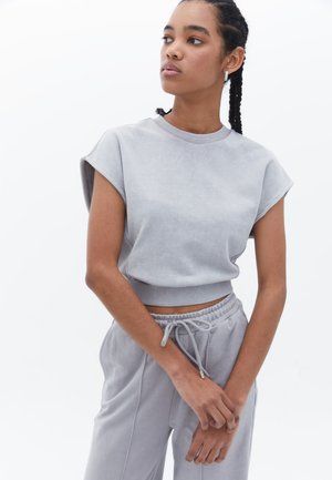 Sudadera recortada gris claro con mangas cortas y ribete en el dobladillo, combinada con pantalones de chándal gris a juego, ambos en suave material de algodón.