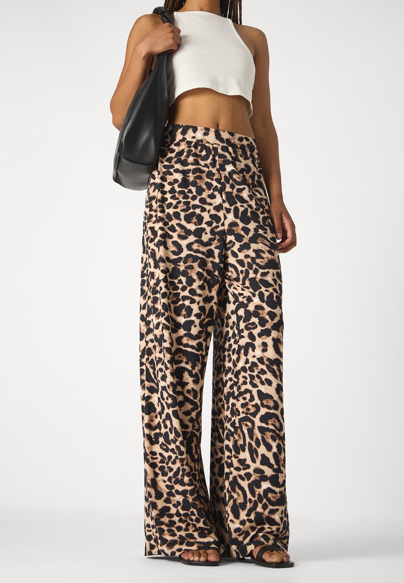 Pantalons larges à imprimé léopard en tissu doux, avec une palette de couleurs noir et beige. Associés à un top court blanc et un sac noir.
