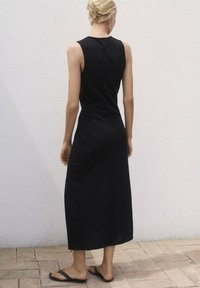 Zwarte mouwloze maxi-jurk met een getailleerde top en een vloeiende rok. Lichtgewicht stof, gladde textuur en midi-lengte, gecombineerd met platte sandalen.