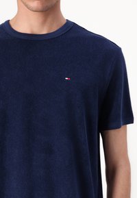 Mann, der ein navyblaues kurzärmliges T-Shirt aus Frottier trägt, mit kleinem rot-, weiß- und blauem Logo auf der linken Brust.