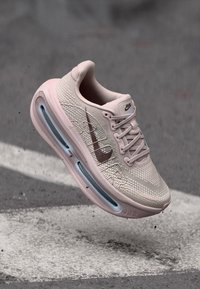 Αθλητικό παπούτσι ανοιχτό ροζ με υφή στο επάνω μέρος, διαθέτει καφέ λογότυπο, διαφανή αερόσφαιρα στη σόλα και τονισμένες αποχρώσεις.