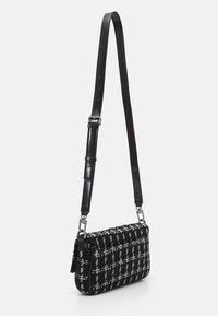 Sac à main en tweed à motifs écossais noir et blanc, avec une bandoulière en cuir noir brillant détachable et des accessoires métalliques. Forme rectangulaire, fermeture à rabat.