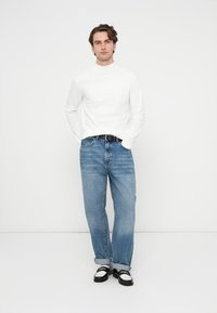 Biała koszula z długim rękawem zestawiona z jasnoniebieskimi, luźnymi dżinsami. Stylizację uzupełnia czarny pasek oraz czarno-białe buty.