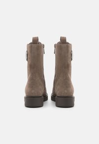 Stivaletti in suede marrone con chiusura a zip laterale, punta rotonda e tacco impilato. Presentano un piccolo anello sul retro per una facile vestibilità.