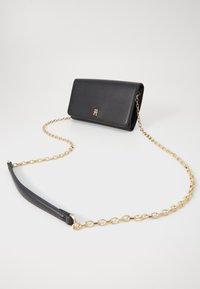 Sac en cuir noir à bandoulière avec une chaîne en or et un détail de logo. Dispose d'une fermeture à rabat et d'une finition lisse et texturée.