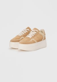 Baskets en daim beige avec une semelle large, accents crème et lacets ronds. Présentent un dessus texturé et une base chunky.