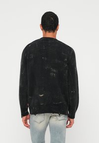 Fekete kötött pulóver texturált felülettel, raglán ujjakkal és bordázott szegéllyel, hátulnézetből. Láthatóak rajta kopott részletek.