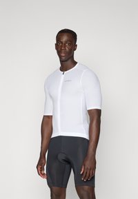 Kurzärmliges Herren-Radsporttrikot aus strukturiertem weißem Stoff mit Reißverschluss vorne und Logo. Kombiniert mit schwarzen enganliegenden Shorts mit Polsterung.