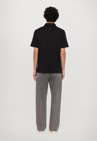 Svart kortermet polo skjorte kombinert med lysegrå vide jeans, med en avslappet passform og mykt bomullsmateriale. Enkelt design, uten mønster.