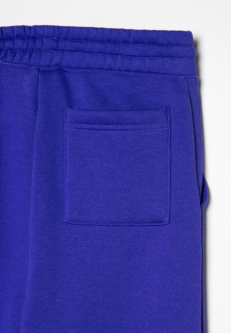 Lila Jogginghose aus weichem Stoff, mit elastischem Bund und einer aufgesetzten Tasche auf der Rückseite. Glatte Textur und gleichmäßige Farbe.