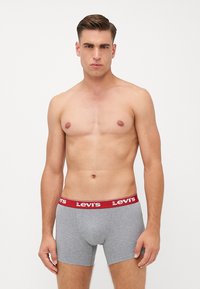 Sive bombažne hlačke s kratkimi nogavicami z rdečim elastičnim pasom, na katerem je logotip Levi's. Gladka tekstura, prilega se telesu in srednje dolga oblika.