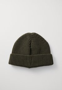 Beanie lavorato a maglia color verde oliva con texture a coste e risvolto. La parte superiore presenta una forma arrotondata con cuciture verticali.