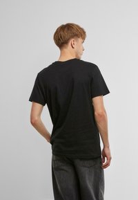 Svart bomull t-skjorte med rund hals og korte ermer, med et enkelt, uprydet design, vist fra baksiden.
