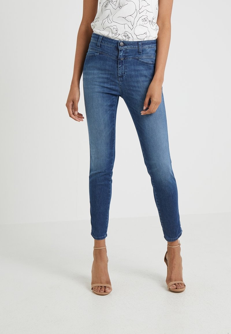 Smala blå jeans i denim med medelhög midja, med en klassisk femfickdesign och subtila blekningar, bärs med nude högklackade sandaler.