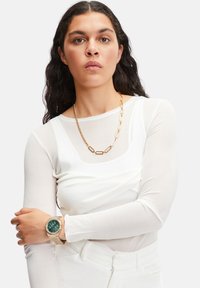 Hvid langærmet top med rund halsudskæring. Guldkæde, linksdesign. Uret har en grøn skive med guldhardware.