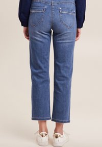 Lichtblauwe denim jeans met een rechte snit, voorzien van twee achterzakken en afgewerkte zomen. Gecombineerd met witte sneakers met gouden accenten.