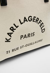 Torba płócienna z czarnym nadrukiem tekstu: "KARL LAGERFELD PARIS" oraz "21 RUE ST-GUILLAUME" na beżowym tle z czarnymi akcentami.